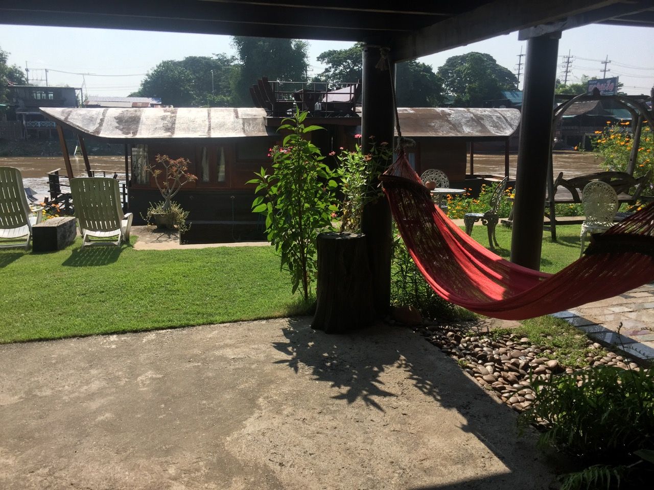 A hammock under a deck, with a river and boat house behind it.