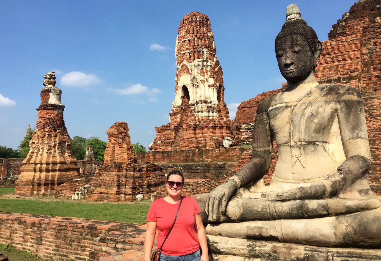 Woman posing in front of ruins including a Buddha statue.