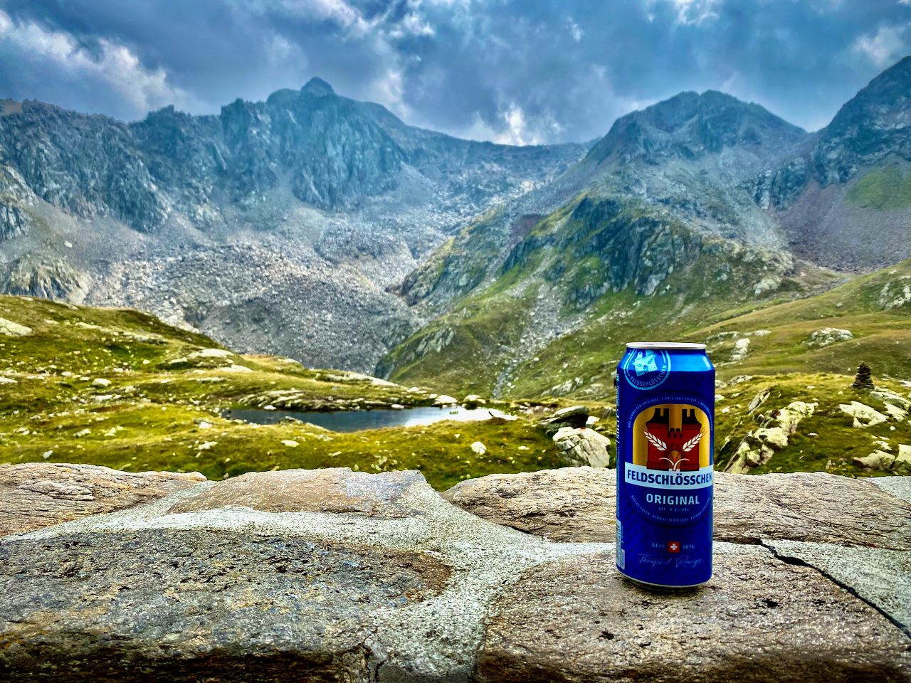 A can of Feldschlösschen beer sitting on a stone wall with mountains in the background.