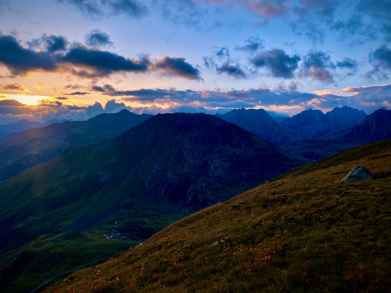 The sun rises above a mountain range with a cloudy sky.