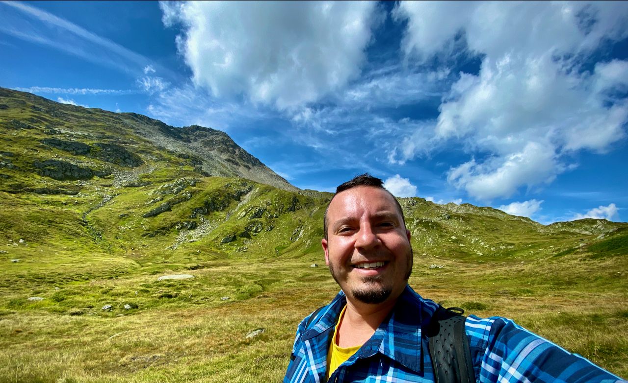 A selfie of Chris with the mountain he just climbed in the background.
