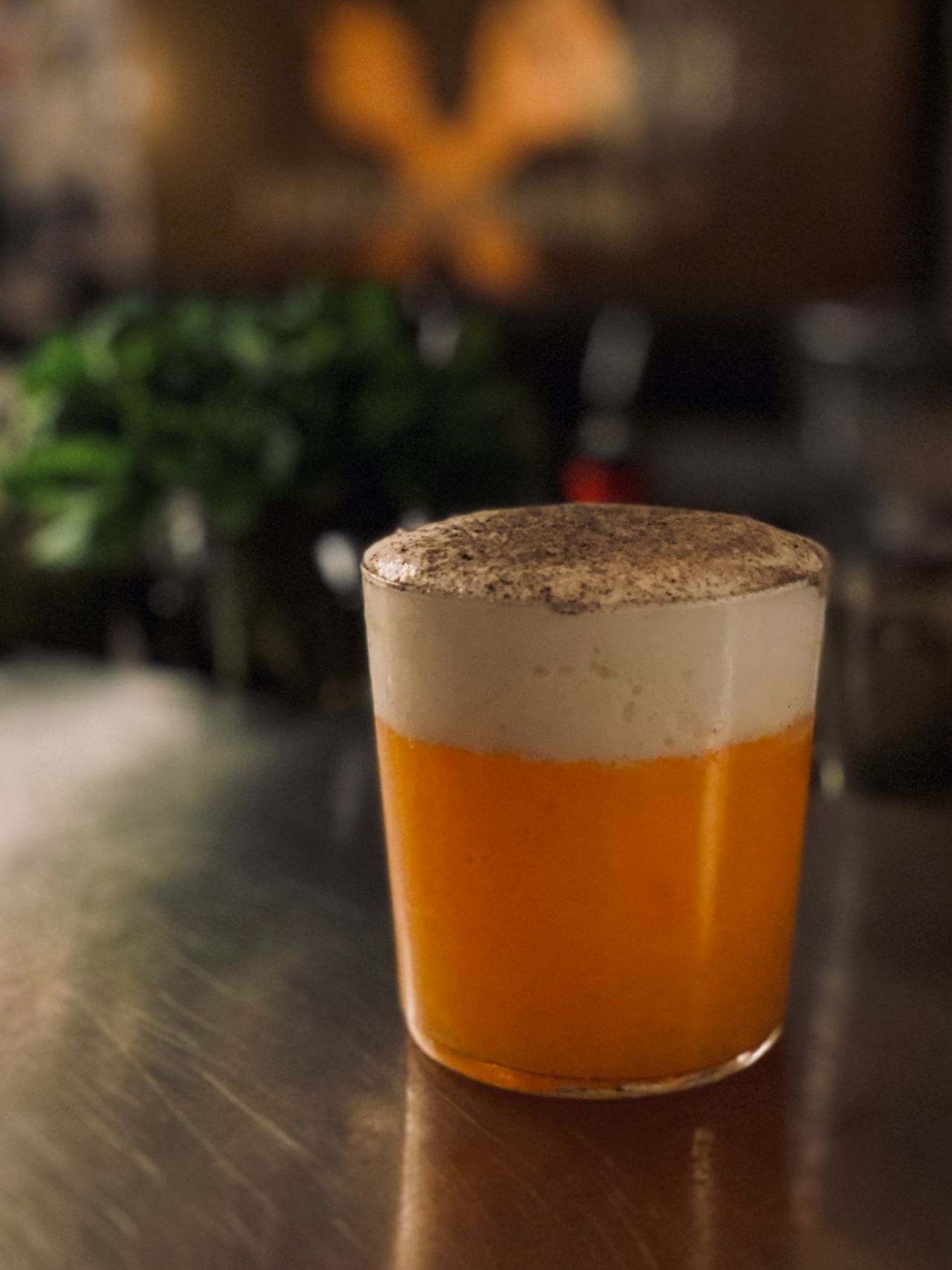 A portrait photo of a light orange colored cocktail with foam head.