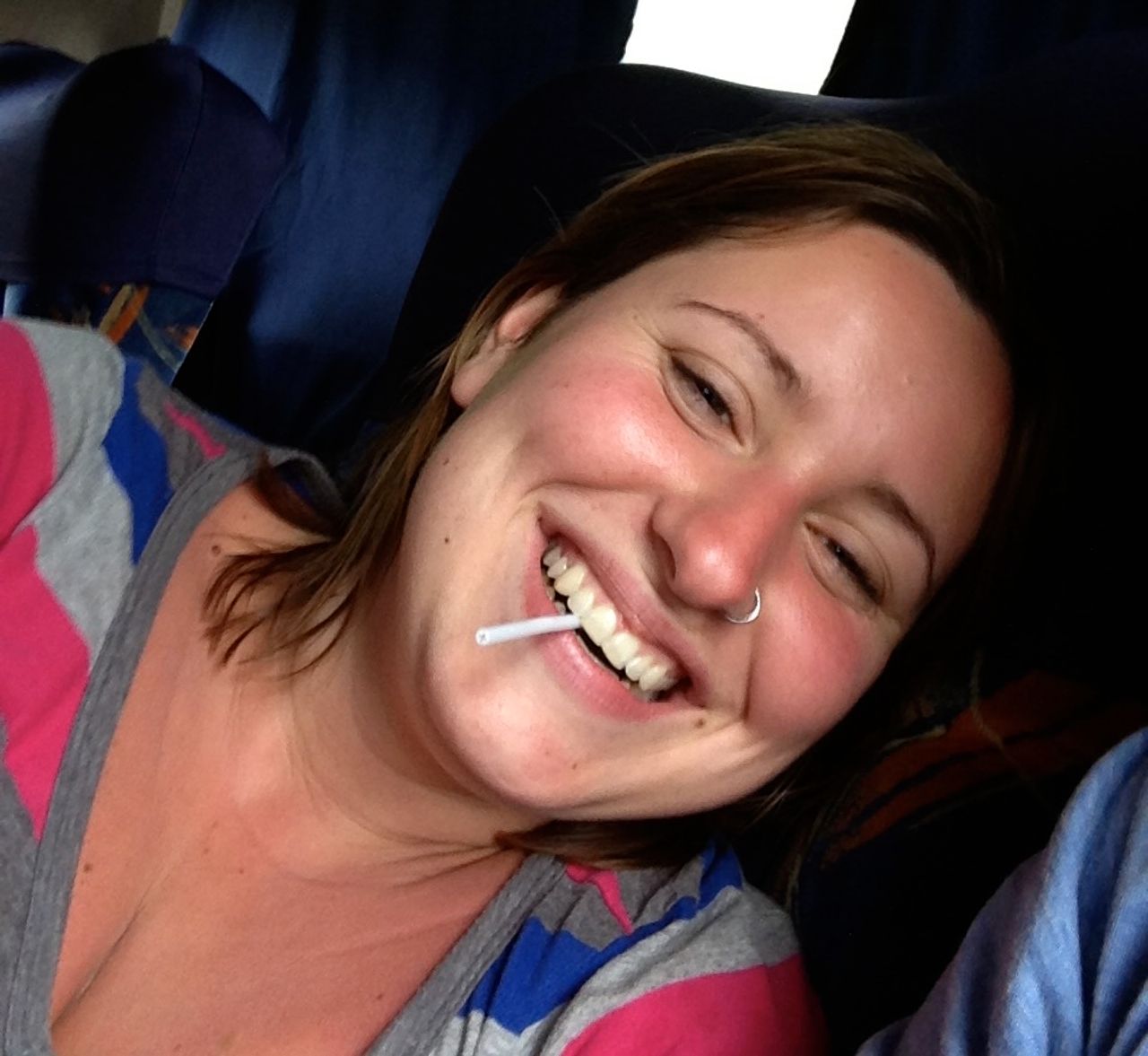 A woman smiling with a lollipop stick in her mouth.