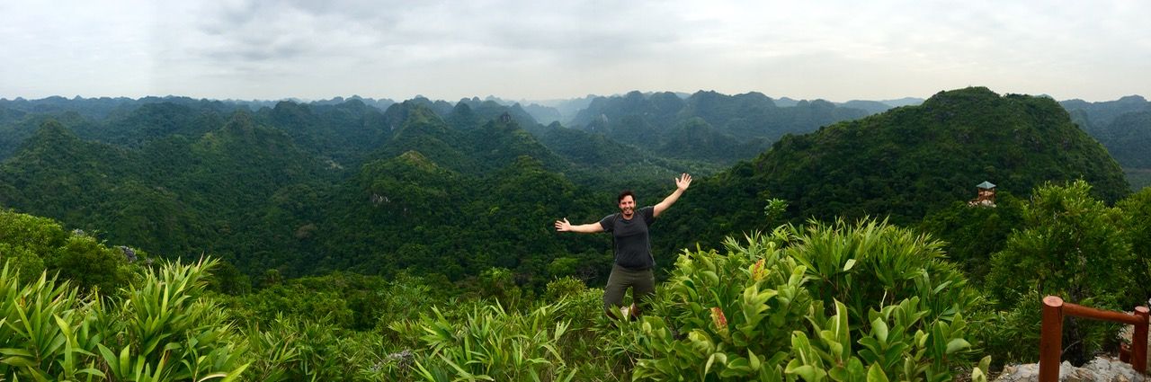 Man posing for camera with jungle-covered mountain range in background.