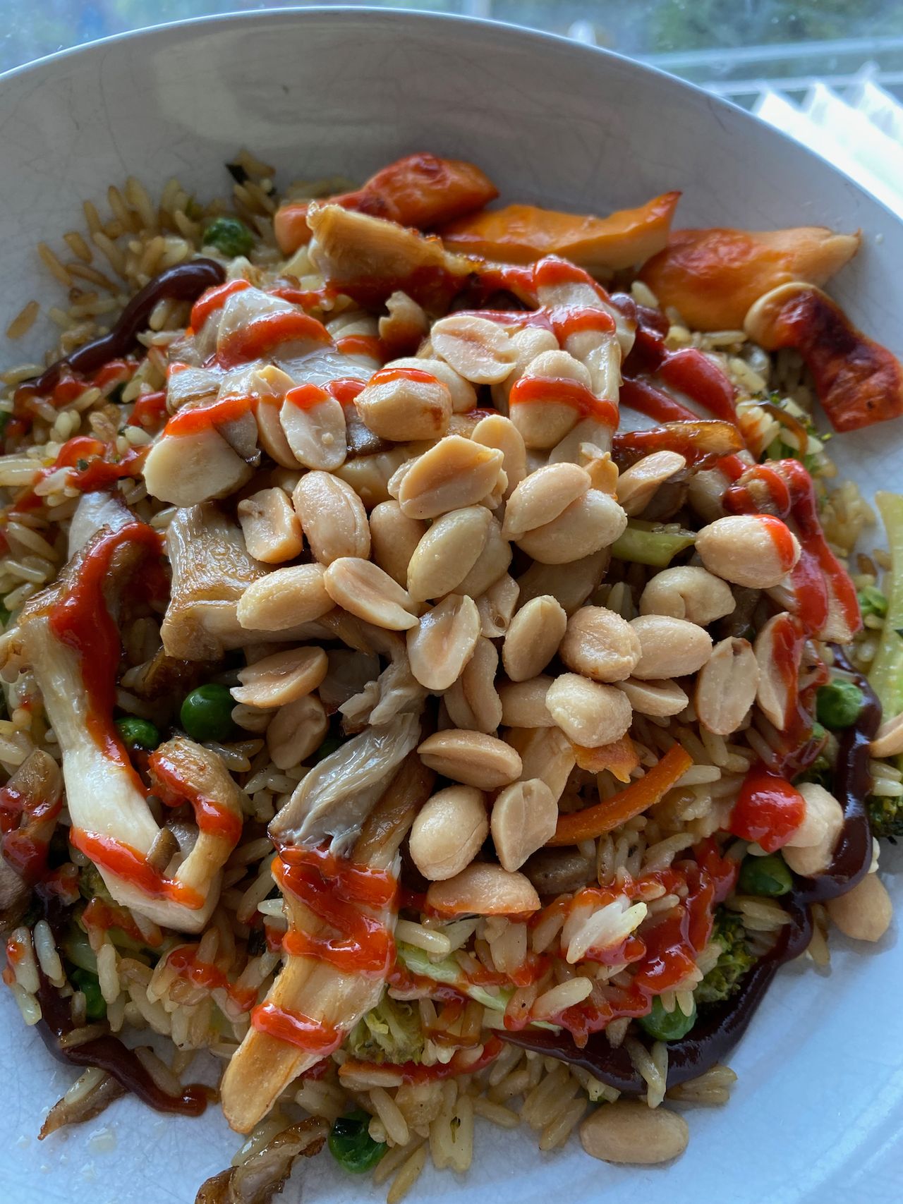 A plate of fried rice with vegetables, topped with peanuts and red sriracha sauce.