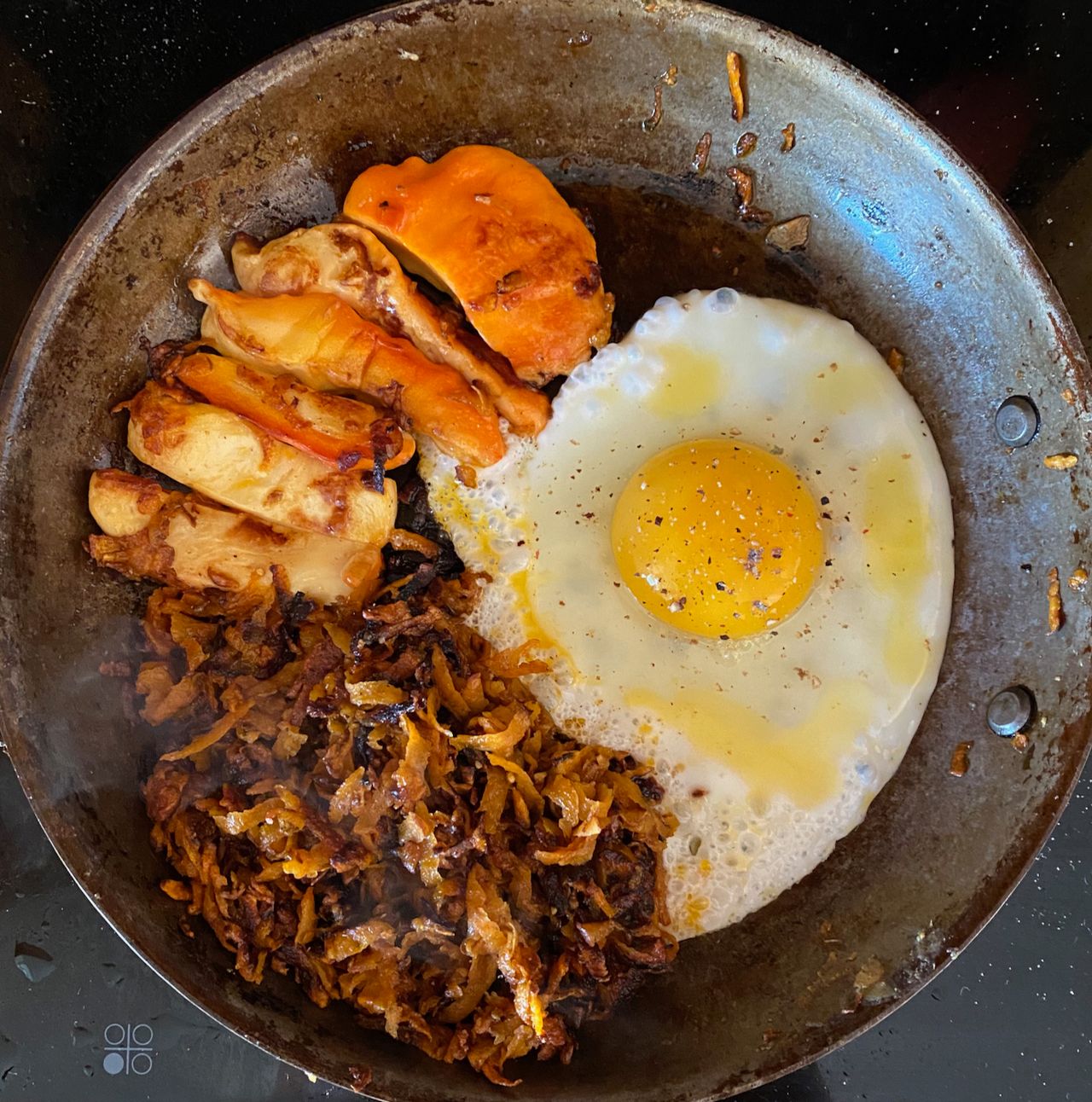 A top-down photo of a skillet on a stove, with a sunny-side up egg, strips of orange mushroom being cooked, and some hash browns being fried.