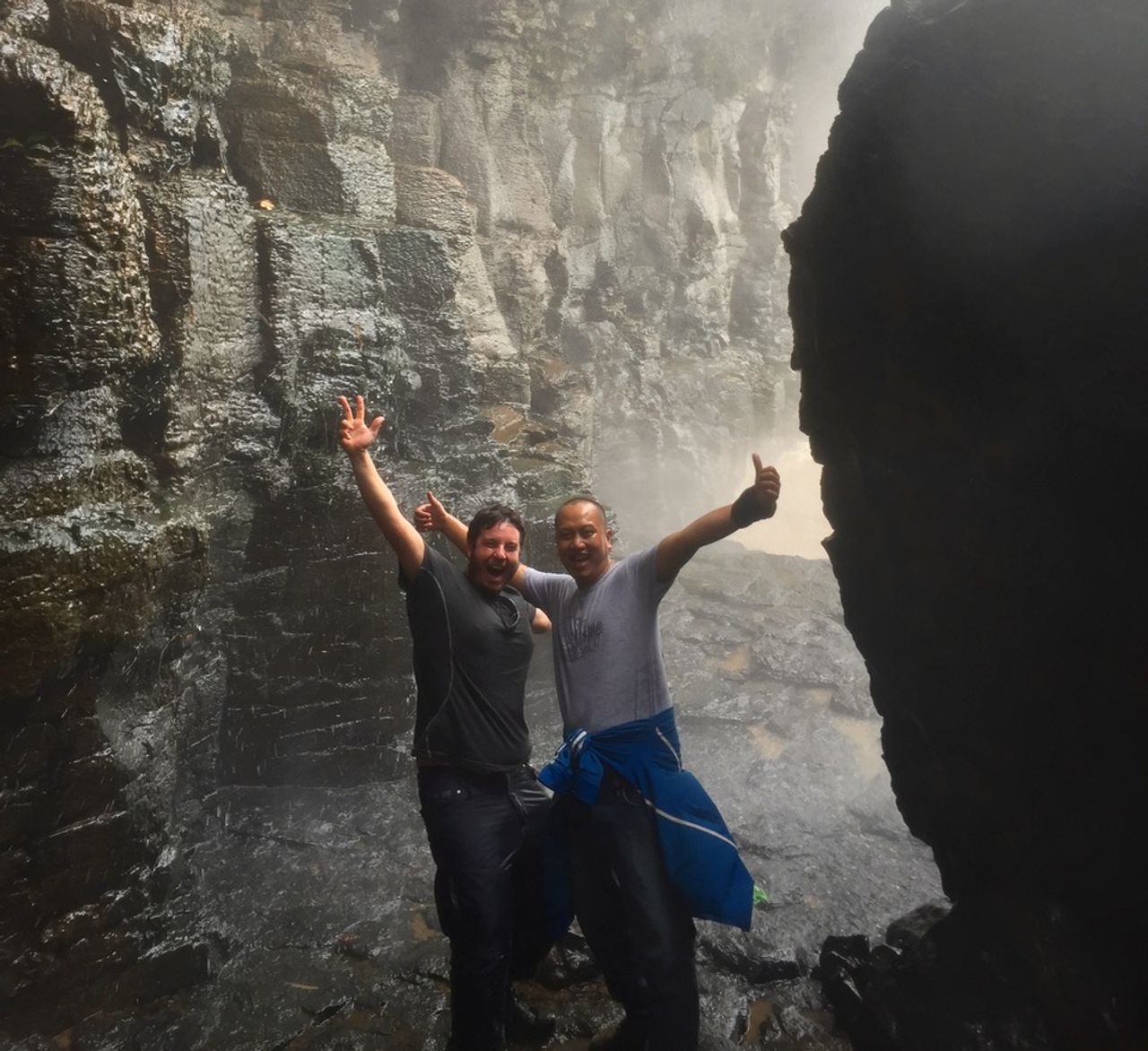 Two men standing behind a waterfall.