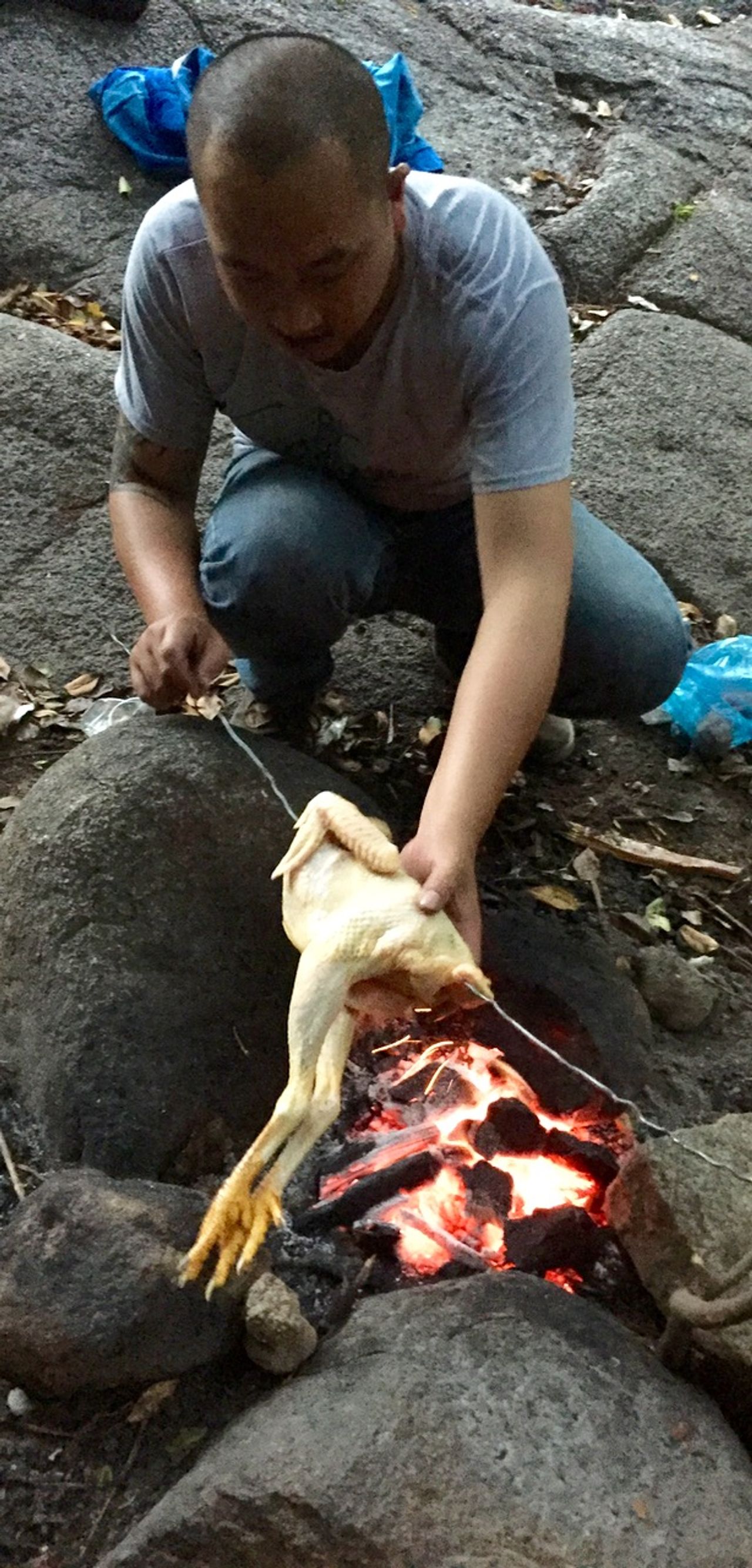 Man skewering a whole chicken over a fire.