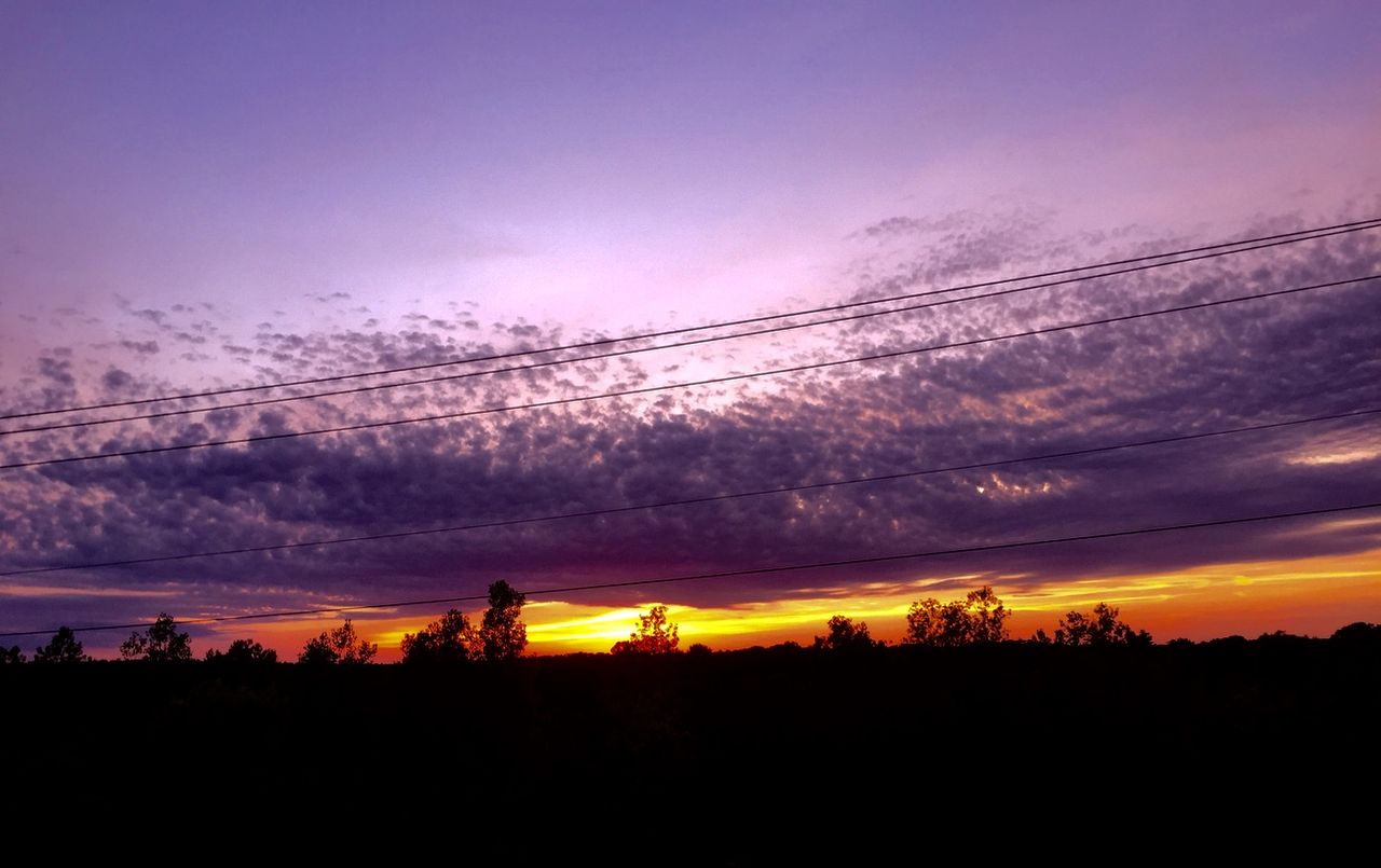 Orange sun setting behind bright purple clouds.