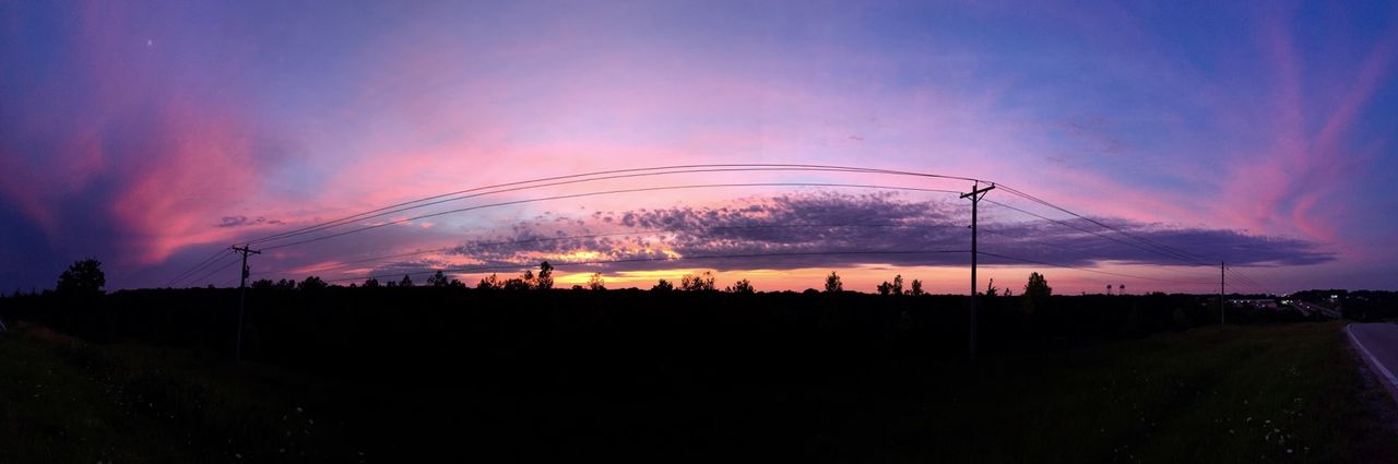 Panoramic of sunset with tall pink clouds on the left and right.