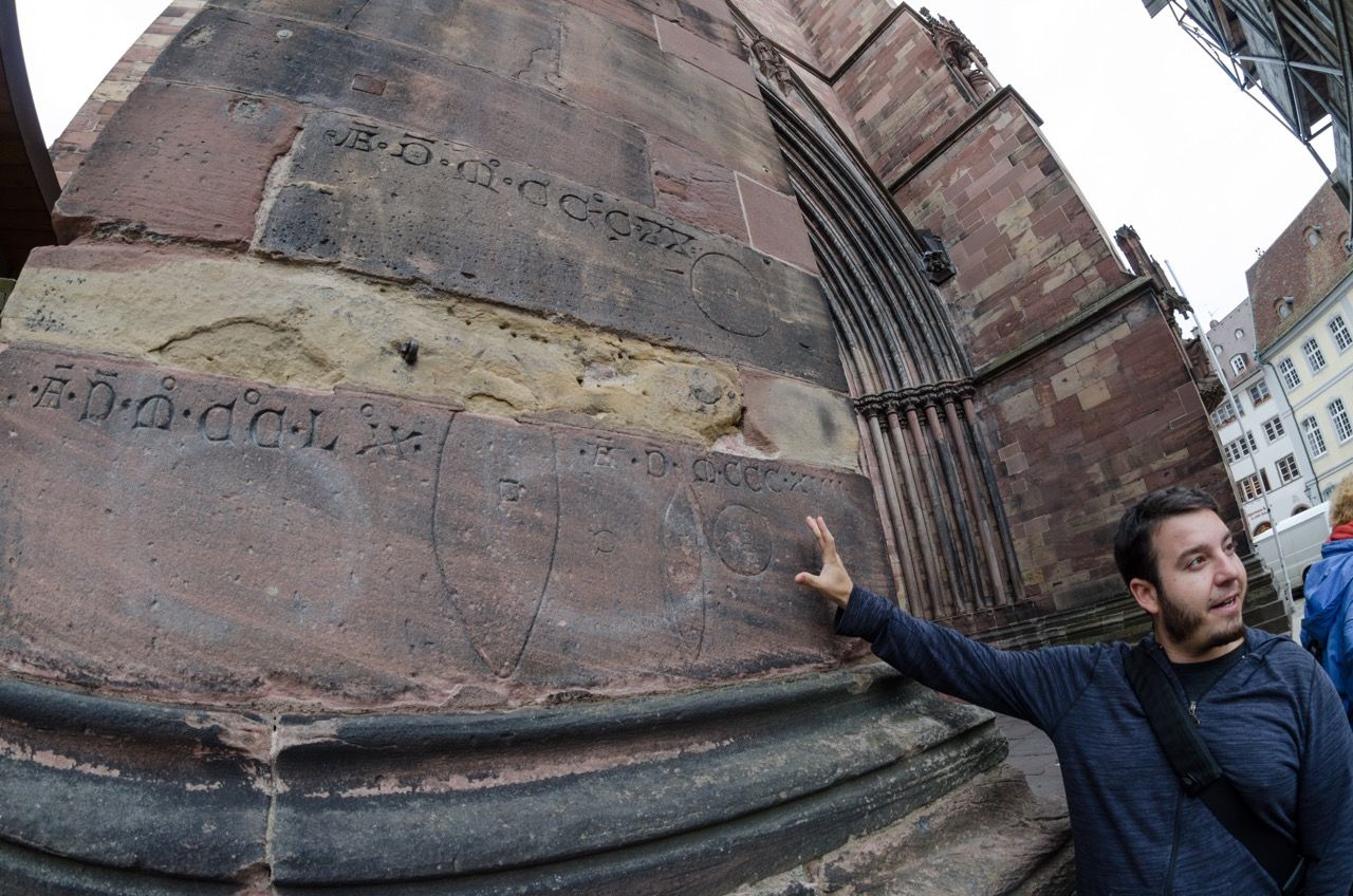 Man explaining symbols etched into a stone wall.