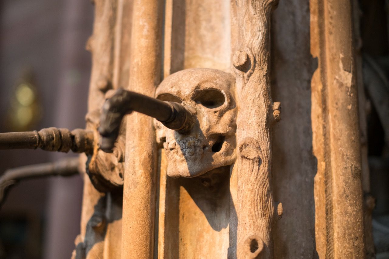 Stone carving of a skull with a fountain pipe coming out of the nose.