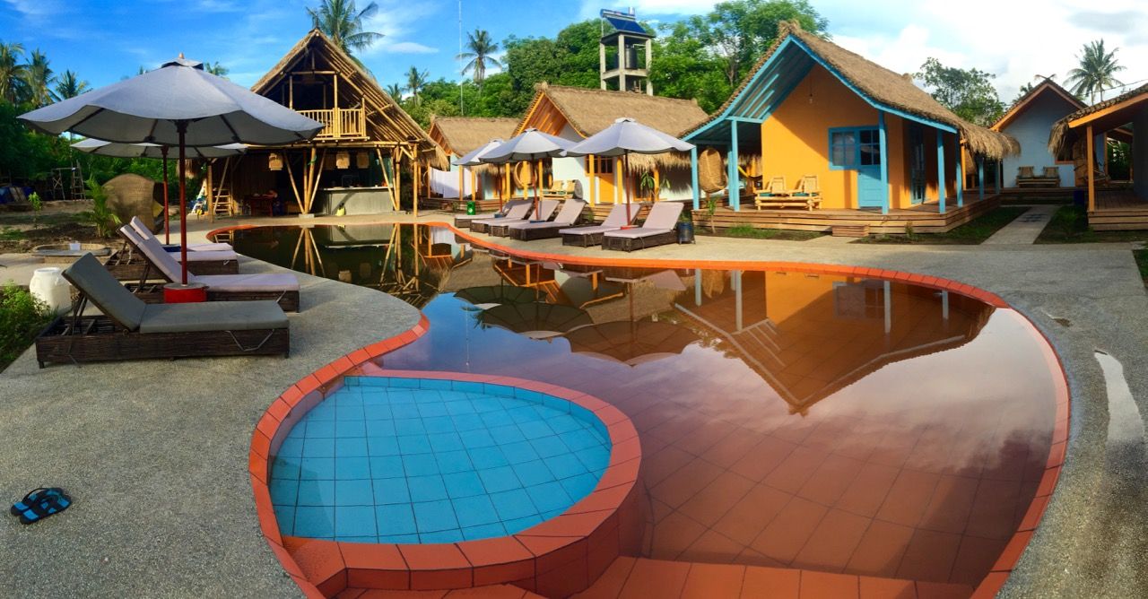 Panoramic of a pool with bungalows in the background.