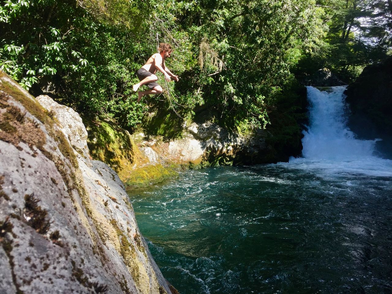 Man jumping into river from a tall rock.