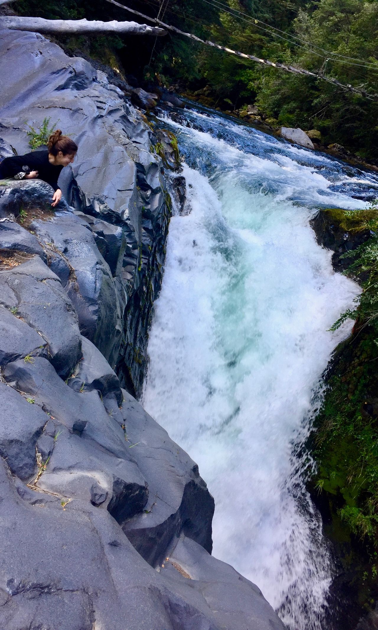Woman laying on her stomach looking at steep waterfall.