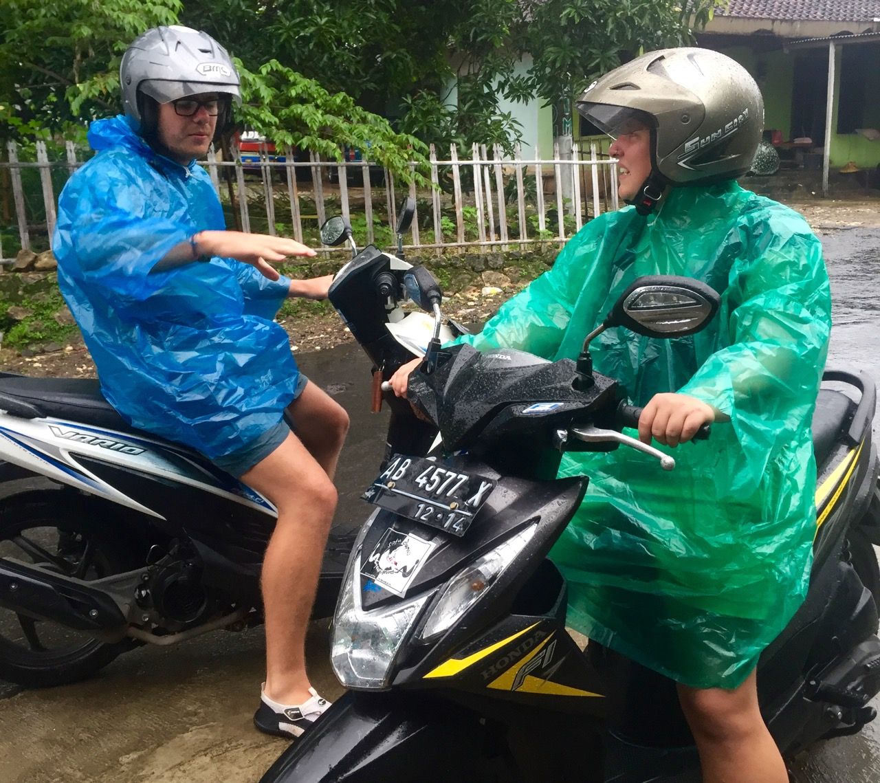 Man and woman with ponchos on motorbikes talking.