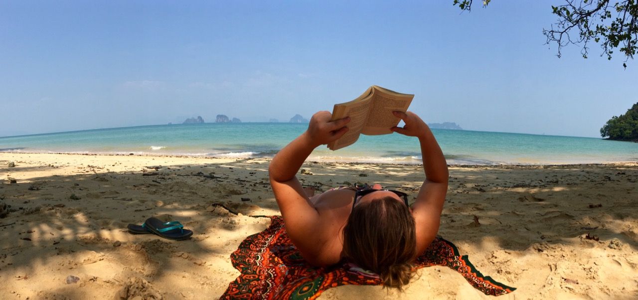 Woman laying on an empty beach reading a book.