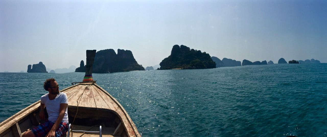 Man looking off the front of a boat driving towards distant islands.