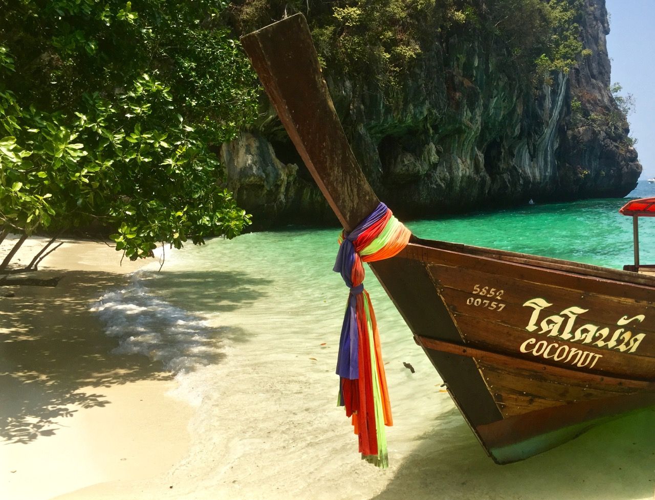 Thai boat named "Coconut" anchored at a beach cove.