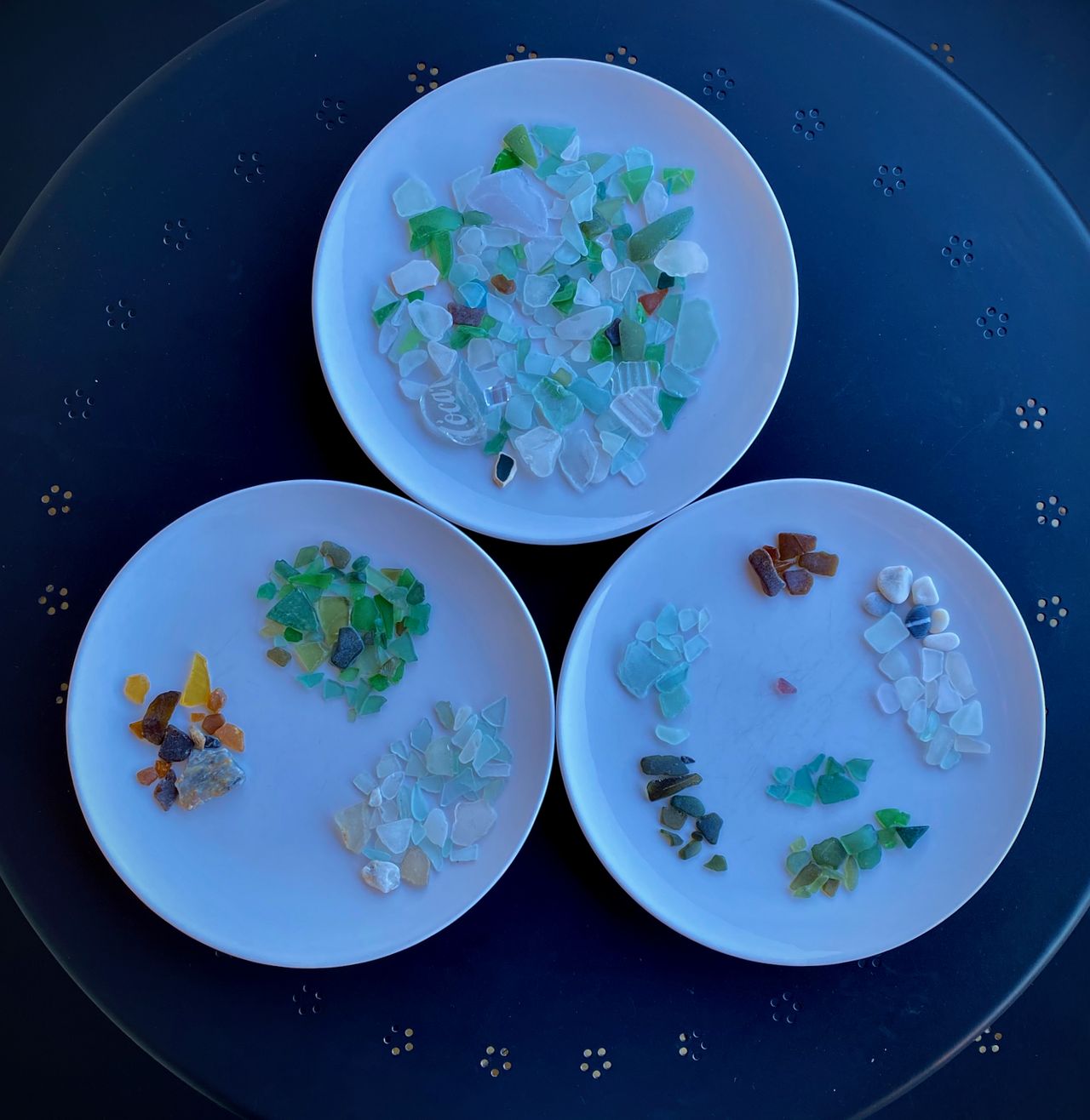Two plates with beach glass arranged by color, and one plate with all the pieces mixed together