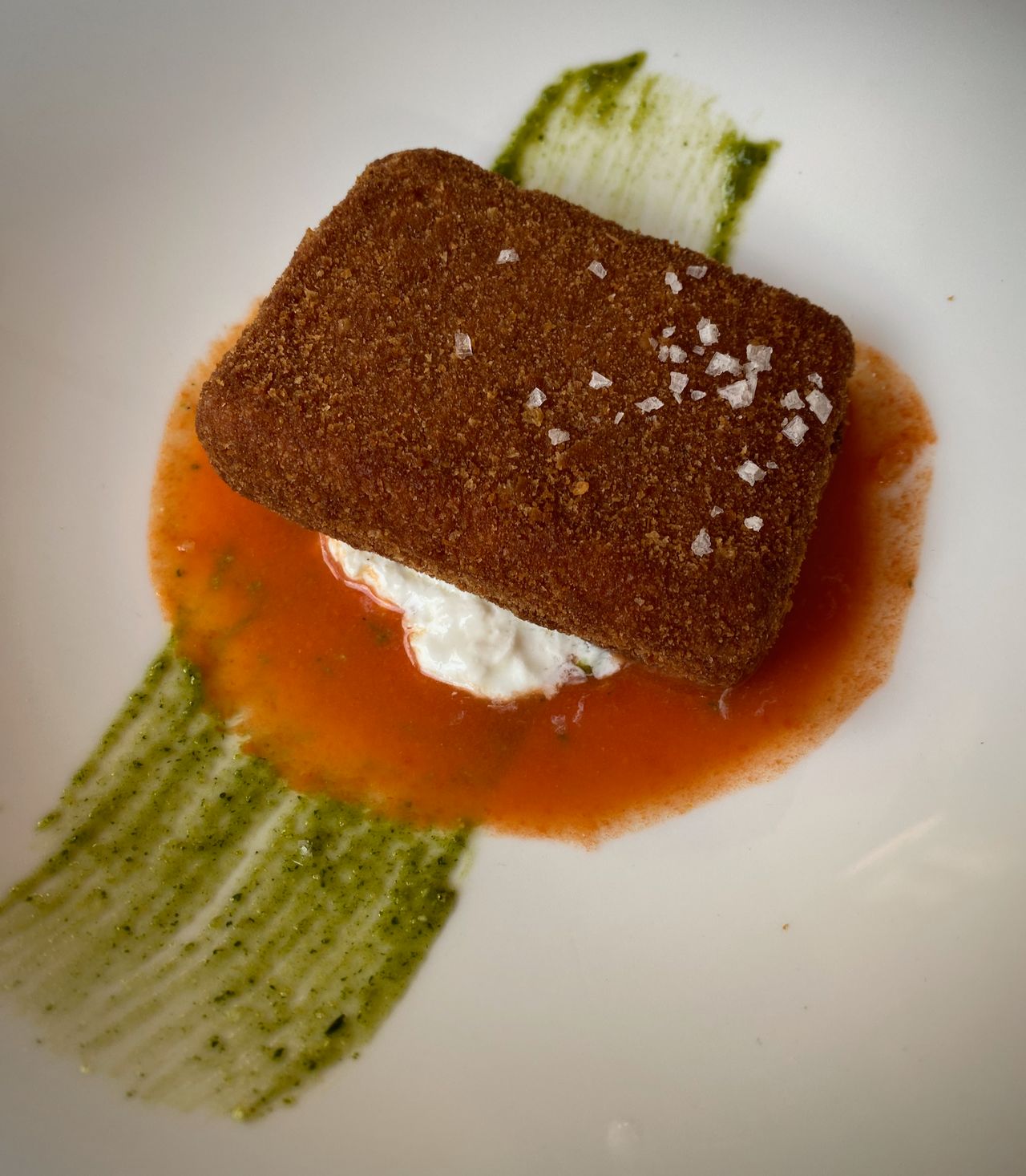 Fried buffalo mozarella sitting on pesto and tomato gazpacho on a white plate