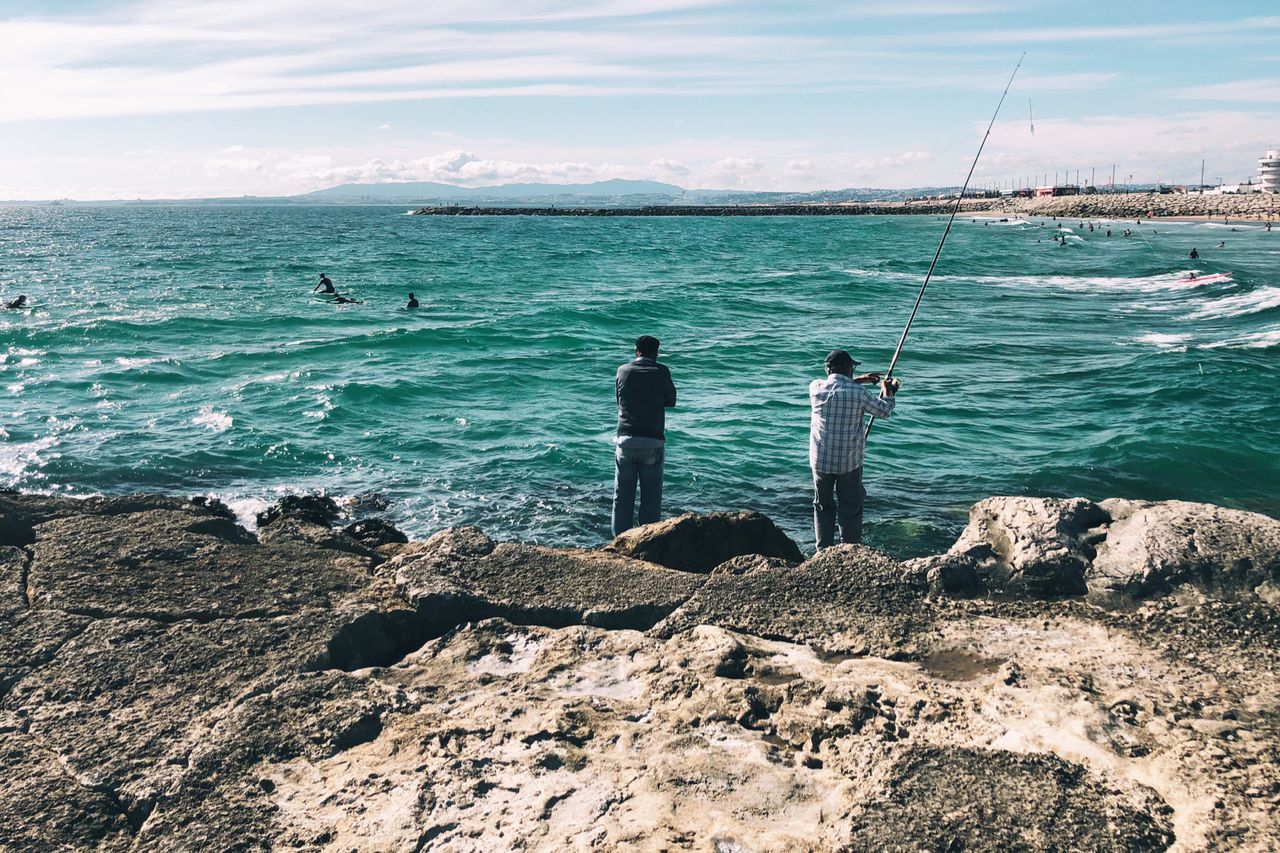 Two men fishing in the ocean upon some rocks.