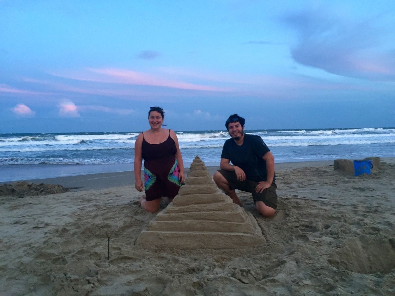 Man and woman posing with sandcastle.