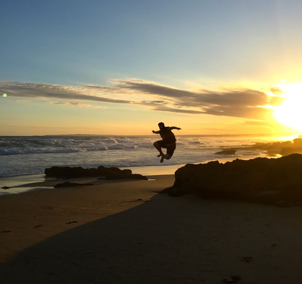 Man's silhouette jumping off a rock.