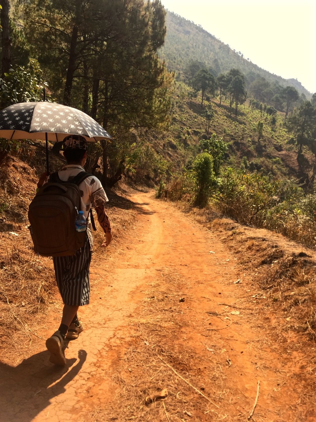 Man walking along dirt road with sun umbrella.