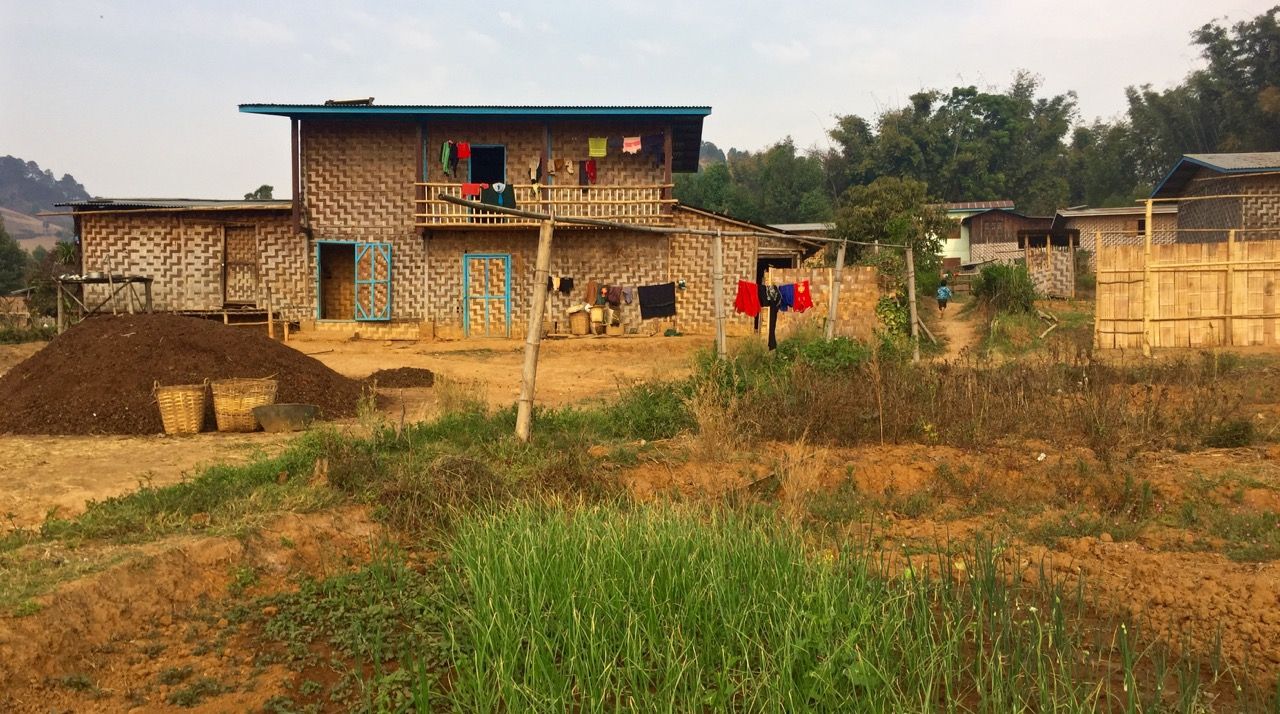 A large village hut with fields in front of it.