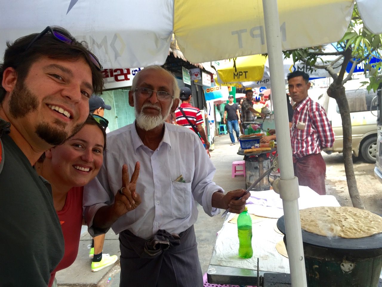 Three people smiling into camera with roti being grilled next to them.