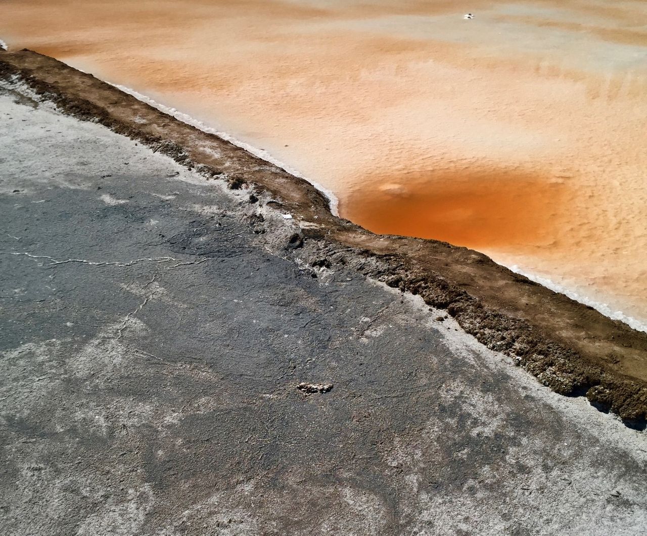 Two pools separated by a path. One is dried grey mud and one is bright orange water with salt.