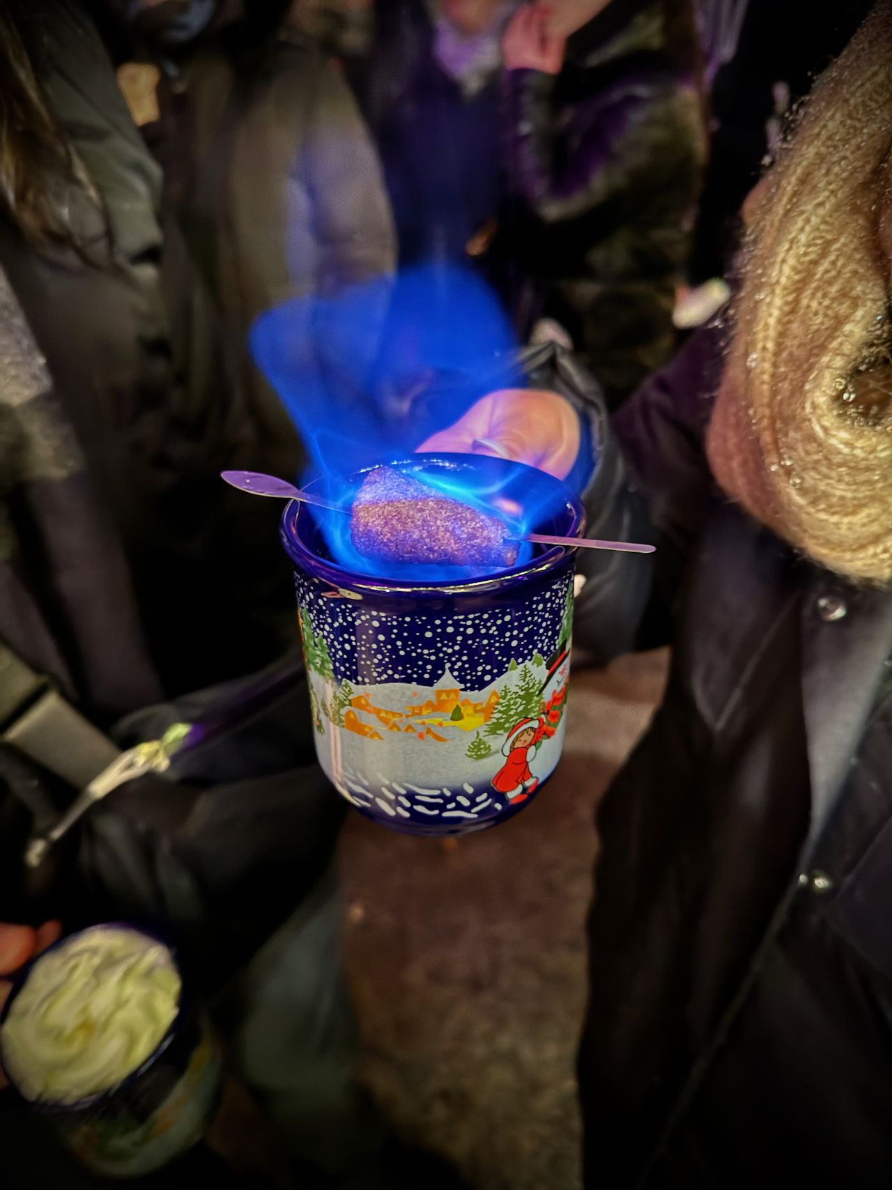 Close-up of the Feuerzangenbowl, a hot drink with a sugar stick on top which has been set on fire. There is a deep blue flame coming off of the sugar.