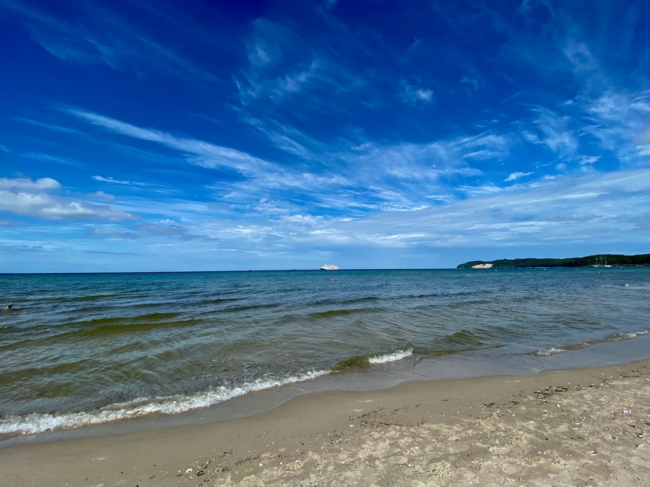 Small waves rolling onto the beach with higher land in the background.