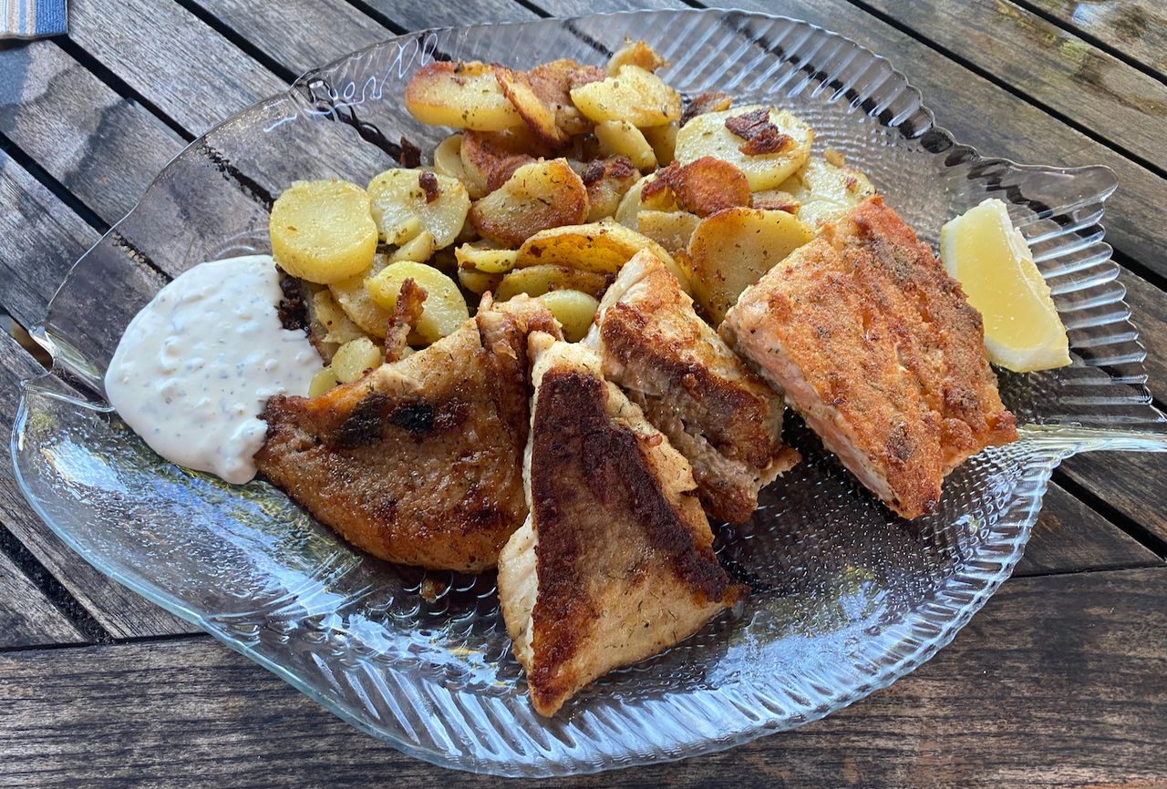 Fried pieces of fish with fried potatoes and a white remoulade.