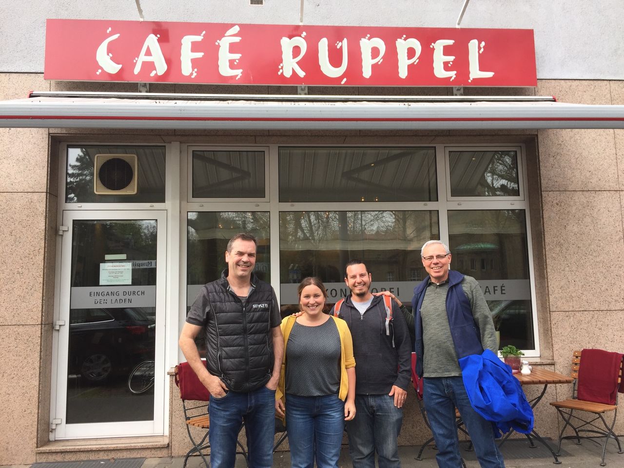 People smiling near a storefront that reads 'Ruppel Café'