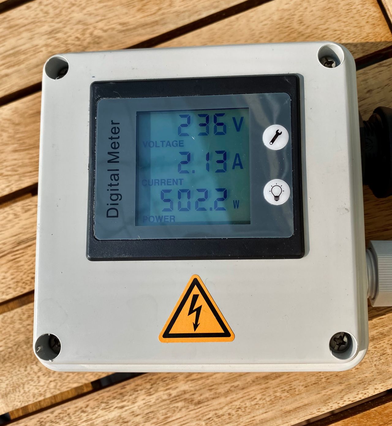 A digital meter for solar panels laying on a wooden table. The meter reads Voltage 236V, Current 2.13A, Power 502.2W
