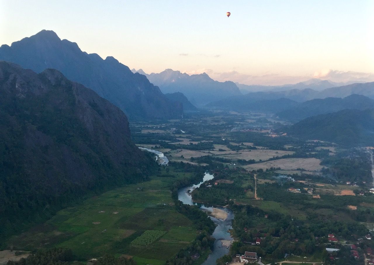 Wide view of a valley with other balloons in the sky.